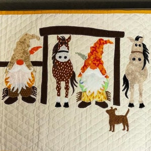 May include: A white quilted wall hanging with a yellow border features a scene of five gnomes standing in front of a wooden fence with four horses. The gnomes are wearing colourful hats and have white beards. The horses are brown, white, and black. A small brown dog is in the foreground.