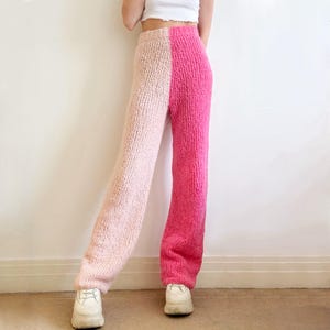 May include: A pair of wide-leg pants with a pink and light pink color block design. The pants are made of a soft, fuzzy material.