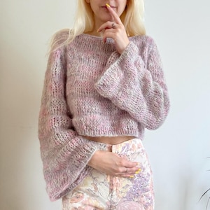 Puede incluir: Un suéter de punto suave de color rosa y blanco con mangas acampanadas. El suéter es corto y tiene un corte holgado.