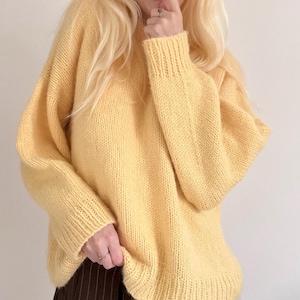 May include: A light yellow, oversized knit sweater with ribbed cuffs and hem. The sweater has a relaxed fit and a soft, textured appearance. The sleeves are long, and the neckline is a classic crew neck.