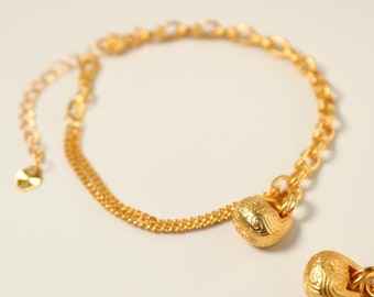 Peut inclure: Un bracelet en chaîne dorée avec deux breloques décoratives. Les breloques sont rondes et ont une surface texturée. Le bracelet est composé de deux chaînes, l'une plus épaisse que l'autre.