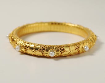 Peut inclure: Un bracelet jonc en or avec un motif floral délicat et des accents de perles blanches.