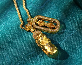 Peut inclure: Deux colliers en or avec pendentifs. Un pendentif est un cadre rectangulaire avec des pierres claires et un petit motif en or à l'intérieur. L'autre pendentif est une figurine en or détaillée avec des pierres claires.