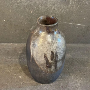 Puede incluir: Un pequeño jarrón de cerámica gris oscuro con un esmalte blanco y marrón. El jarrón tiene un cuerpo redondeado y un cuello estrecho.