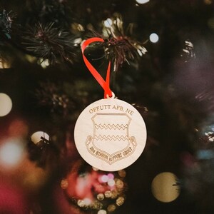 May include: A wooden Christmas ornament with a red ribbon. The ornament is round and has a brown wood grain. It is decorated with the text "Offutt AFB, NE" and "35th Mission Support Group".