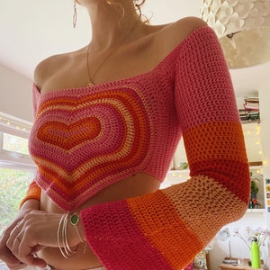Puede incluir: Un top de crochet rosa, naranja y melocotón con un diseño en forma de corazón y mangas acampanadas.