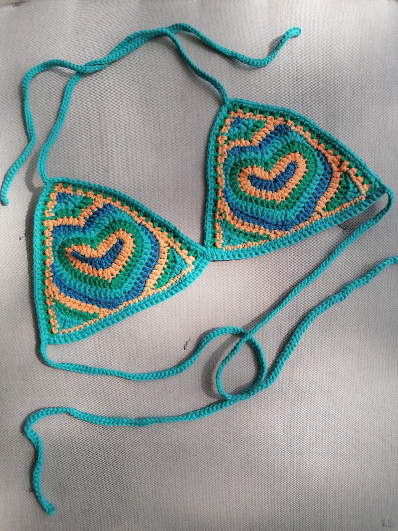 May include: A teal blue crocheted bikini top with a geometric pattern in shades of green, orange, and blue.