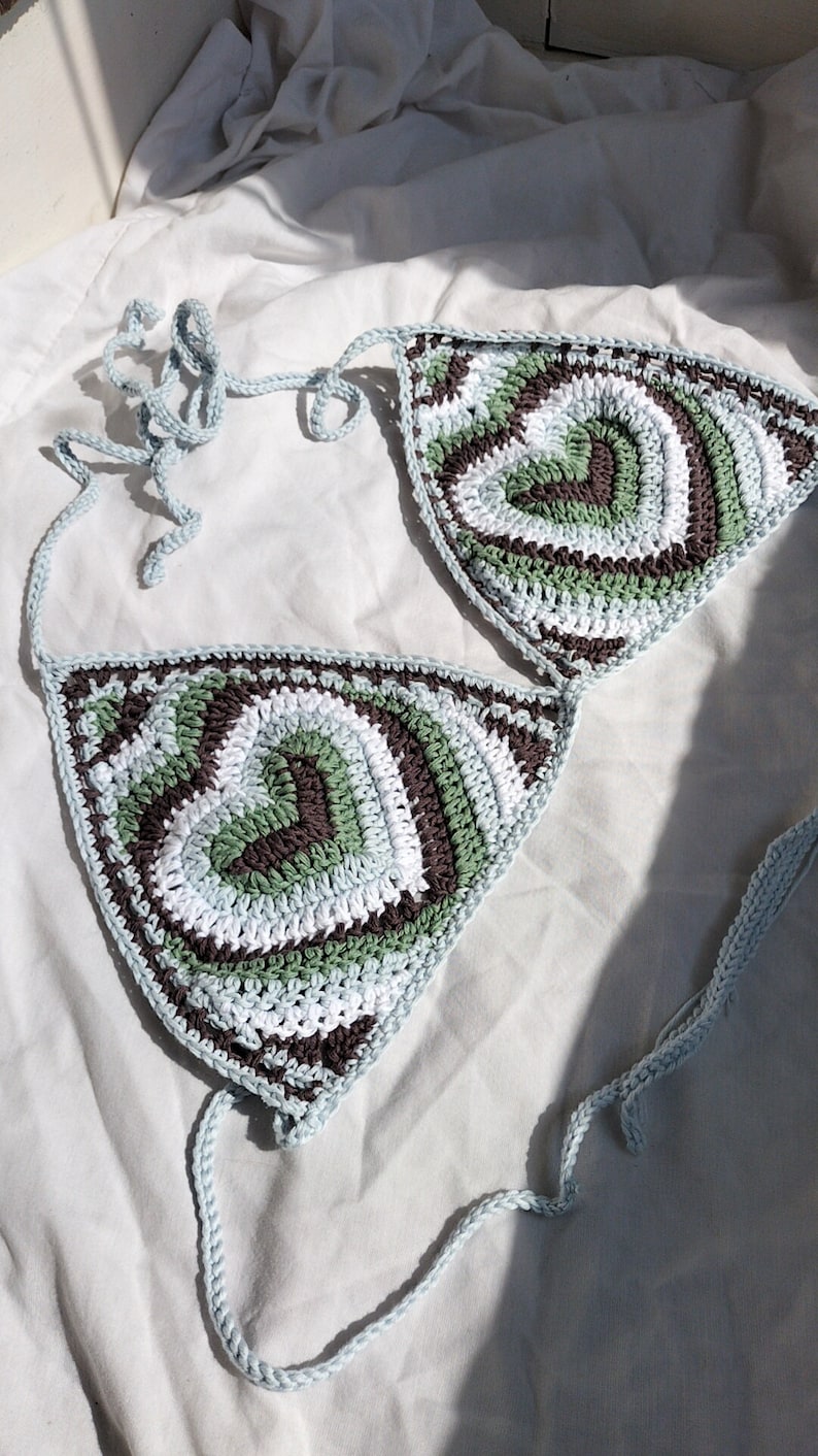 May include: A crocheted bikini top with a light blue, white, green, and brown color pattern. The top is made of a soft, lightweight yarn and has a triangular shape.