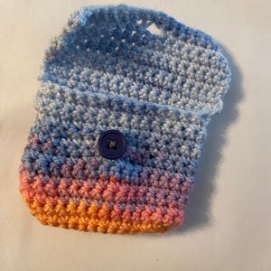 May include: A small crocheted pouch with a blue, purple, and orange ombre design. The pouch has a flap that closes with a blue button.