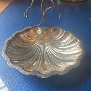 May include: A silver shell-shaped dish with a decorative metal stand. The dish has a scalloped edge and a raised centre.