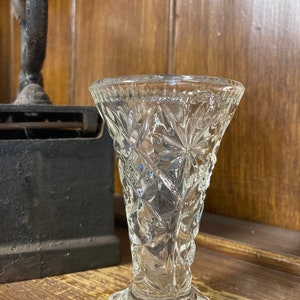 May include: A clear glass bud vase with a cut glass design. The vase has a wide mouth and a narrow base.