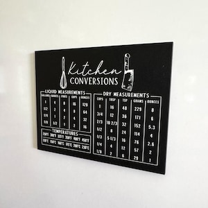 May include: Black kitchen conversion chart with white text. Includes liquid and dry measurements, and temperature conversions. Features illustrations of a whisk and a knife. Measurements are in gallons, quarts, pints, cups, ounces, and Fahrenheit.