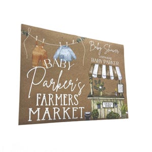May include: A brown card with the text "Baby Parker's Farmers Market" in white script. The card features illustrations of baby clothes hanging on a washing line and a farmers market stall. The words "Baby Shower celebrating Baby Parker" are also present.