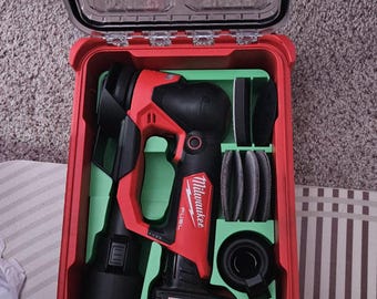 Könnte beinhalten: Ein roter Milwaukee Packout Aufbewahrungskoffer mit transparentem Deckel und Milwaukee-Logo. Im Inneren befindet sich ein rot-schwarzes Milwaukee M12 Fuel Akku-Werkzeug mit Akku, eingebettet in eine grüne Schaumstoffeinlage mit runden Pads.