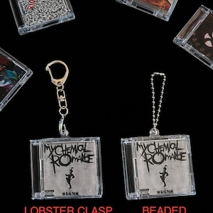 May include: Clear plastic keychain featuring a miniature CD case with the band name "My Chemical Romance" in black and white. The keychain is available with a lobster clasp or beaded chain. Other CD case keychains are also visible.