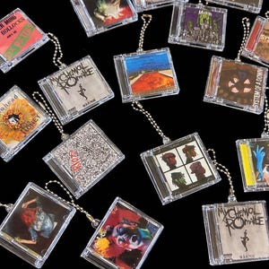 May include: A collection of miniature CD keychains featuring album art from various bands. The keychains are in clear plastic cases with silver ball chain attachments. Album art includes "My Chemical Romance", "Sex Pistols", and "System of a Down".