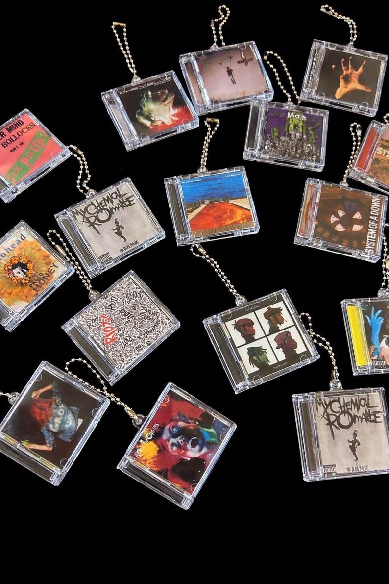 May include: A collection of miniature CD keychains featuring album art from various bands. The keychains are in clear plastic cases with silver ball chain attachments. Album art includes "My Chemical Romance", "Sex Pistols", and "System of a Down".