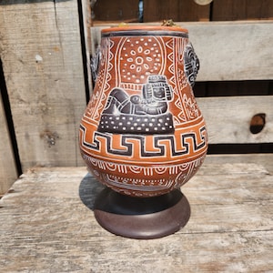 以下が含まれることがあります： 幾何学模様と横たわる人の白黒の絵が描かれた茶色の陶器の花瓶。花瓶は底が広く、首が細い。