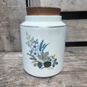 May include: White ceramic jar with a cork lid and a floral design featuring blue, white, and green flowers.
