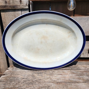 May include: A white oval serving platter with a blue rim. The platter is slightly worn and has a rustic look.