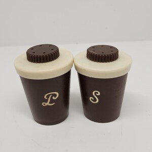 May include: A pair of vintage salt and pepper shakers. The shakers are brown with off-white tops and dark brown, ridged lids. The letter "P" is on one shaker and the letter "S" is on the other.
