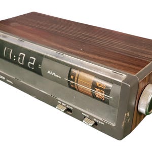 Könnte beinhalten: Vintage Lloyds Digitalwecker mit Holzmaserungsoberteil und grauem Gehäuse. Die Uhr zeigt die Uhrzeit an und verfügt über AM/KHz-Radioeinstellungen und Alarmsteuerungen. Die Uhr ist ca. 20 cm lang.