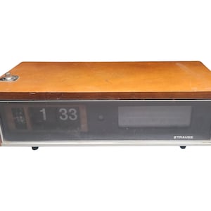 May include: A vintage wooden alarm clock with a digital display showing "1 33". The clock has a rectangular shape with a brown wooden exterior and a black display panel. The brand name "STRAUSS" is visible.
