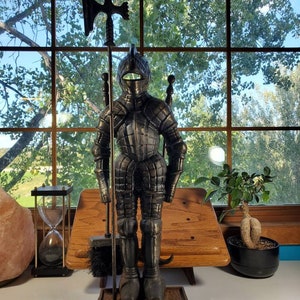 May include: A black metal fireplace tool set featuring a knight in armour holding a poker, a brush, and a shovel. The knight is standing on a base with a decorative design.