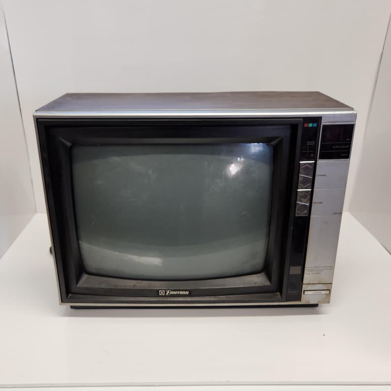 May include: A vintage Emerson television set with a silver and black frame. The screen is dark grey, and the control panel is on the right side. The Emerson logo is visible on the lower left corner. A classic piece of retro electronics.
