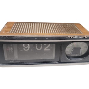 May include: Vintage digital alarm clock with a wood-grain top and a black frame. The clock displays the time as 9:02. It has a round dial on the right side and the words "solid state" are visible on the display.