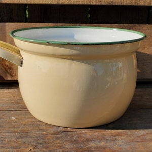 May include: A vintage cream-coloured enamelware pot with a green rim and a single handle. The pot is slightly rounded and has a smooth, glossy finish.