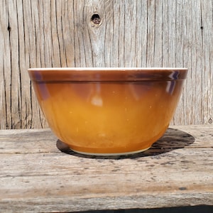 Puede incluir: Un tazón de mezcla de cerámica marrón con un borde blanco. El tazón está sobre una superficie de madera.