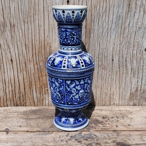 Op de afbeelding: Een blauwe en witte keramische vaas met ingewikkelde bloem- en wijnstokontwerpen. De vaas heeft een brede basis en een smalle hals met een decoratieve bovenkant.