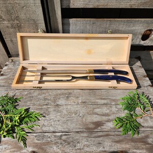 May include: A wooden box containing a blue and gold carving knife and fork set. The box is open and the knife and fork are visible.