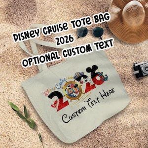 Puede incluir: Bolso tote de lona color crema con el texto "Disney Cruise Tote Bag 2026" y "Optional Custom Text". El bolso presenta un gráfico colorido de Mickey y Minnie Mouse en un timón.