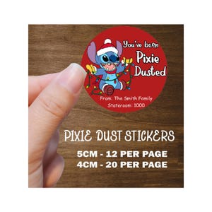 Könnte beinhalten: Ein roter runder Aufkleber mit einer Cartoon-Figur mit Weihnachtsmütze und Lichterketten. Der Aufkleber trägt die Aufschrift "You've been Pixie Dusted" und "From: The Smith Family, Stateroom: 1000". Darunter steht der Text "PIXIE DUST STICKERS".