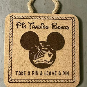 Puede incluir: Un tablero cuadrado para intercambio de pines con asa de cuerda. Presenta el texto "Pin Trading Board" y "Take a Pin & Leave a Pin". Incluye una silueta de Mickey Mouse y un gráfico de un crucero.