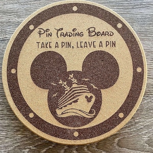 Pode incluir: Quadro redondo para troca de pinos com borda marrom e centro marrom claro. O centro apresenta uma forma de cabeça do Mickey Mouse com uma ilustração de navio de cruzeiro. O texto diz "Pin Trading Board, Take a Pin, Leave a Pin."