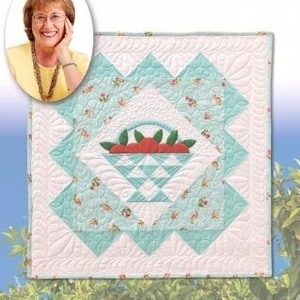 May include: A quilt pattern for a wall hanging featuring a basket of oranges. The quilt is made in a patchwork style with a light blue and white color scheme. The title "Basket of Oranges Wallhanging" is printed below the quilt. The text "Original Design by Ruby McKim" and "Instructions by Eleanor Burns" are printed below the title.