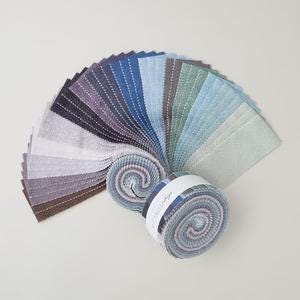 May include: A collection of fabric swatches in a fan shape, showcasing a variety of blue, gray, and neutral tones. Two rolled bundles of fabric are also visible, with a white label wrapped around one. The fabrics appear to be cotton or a similar material.