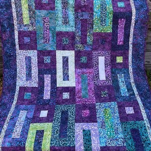 May include: A purple, blue, and green quilt with a geometric pattern of squares and rectangles. The quilt is made of fabric with a batik design.