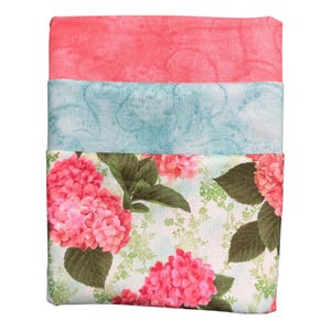 May include: Three folded fabric pieces. The top piece is coral, the middle is light blue with a swirl pattern, and the bottom piece features a floral print with pink hydrangeas and green leaves on a light blue background.