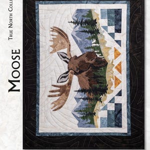 May include: A True North Collection Moose sewing pattern featuring a quilted wall hanging with a moose head, pine trees, and mountain landscape. The design includes a black border and text stating Framed 16" x 22" | Block 11" x 17".