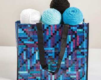 May include: A tote bag filled with yarn balls. The bag has a pixelated design in shades of blue, purple, and pink. The yarn balls are white, light blue, dark blue, and brown. The bag has black handles.