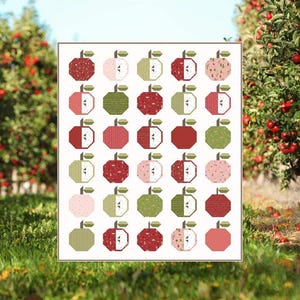 May include: A quilt pattern titled "Apple Season" by Jennifer Long. The pattern features a grid of 36 red, green, and pink apple blocks. The pattern is available in table runner, crib, and lap sizes. The website address is sewastory.com.