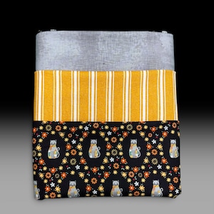 May include: A rectangular fabric pouch featuring three distinct horizontal sections. The top is light gray with a subtle crosshatch texture, the middle is mustard yellow with vertical white stripes, and the bottom is black with a cat and flower print.