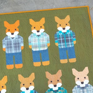May include: A handmade quilt featuring a repeating pattern of stylized foxes. Each fox is depicted wearing a plaid shirt and blue jeans. The quilt has a green background with a wood grain texture and an orange border.
