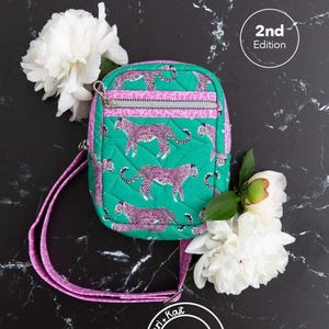 May include: Green crossbody bag with a pink leopard print design, a pink strap, and a zipper closure. The bag is decorated with white flowers and the text "Athena Crossbody" at the top.