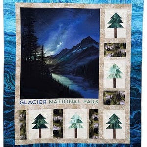 May include: A rectangular quilt featuring a central panel of a night landscape in Glacier National Park with mountains, a lake, and a starry sky. The border includes alternating blocks of green pine trees and black bears on a tan background.