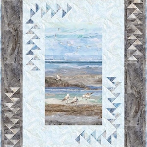 May include: A coastal-themed quilt featuring a seascape with seagulls on a beach. The central image depicts a serene ocean scene in shades of blue and gray. The quilt is framed with a marbled border and triangle accents, creating a textured, artistic design.